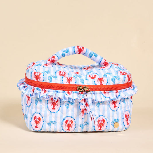 The Darling Effect’s Harbor House Glam & Go Quilted Cosmetic Bag is a rectangular bag with a top handle, red zipper, and ruffled trim, featuring red lobsters and blue seashells on white and blue stripes.