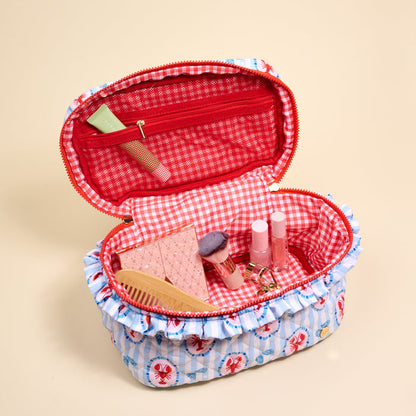 The Darling Effect Harbor House Glam & Go Quilted Cosmetic Bag, featuring a colorful lobster and nautical print, is open to reveal pink gingham lining holding cosmetics, a comb, two lip products, a clip, a tube, and blush with a brush.