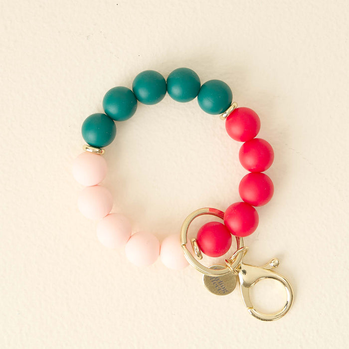 The Darling Effect’s Holly Jolly Hands-Free Keychain Wristlet features pink, red, and teal silicone beads with a gold clasp for a stylish, convenient way to carry your keys.