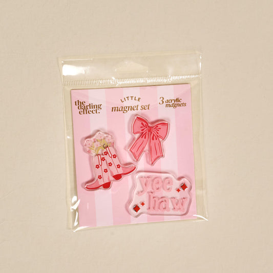 The Darling Effect Howdy Honey Little Magnet Set includes 3 pink acrylic fridge magnets—a floral cowboy boot, bow, and “Yee Haw” word magnet—perfect for decoration, all presented on a pink striped card in a clear bag.