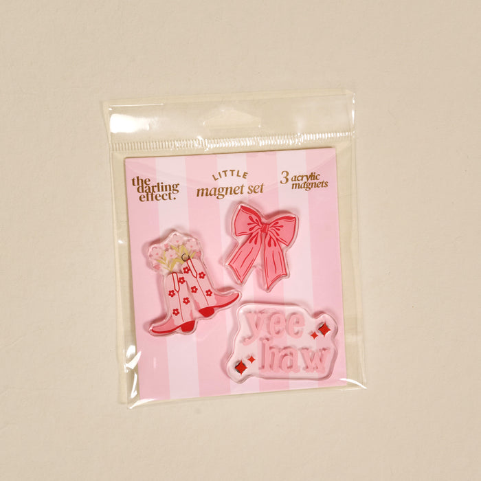 The Darling Effect Howdy Honey Little Magnet Set includes three acrylic magnets—a pink cowboy hat with flowers, a pink bow, and a pink "Yee Haw" sign—ideal as decorative accents or fridge magnets. Packaging reads: LITTLE magnet set 3 acrylic magnets.