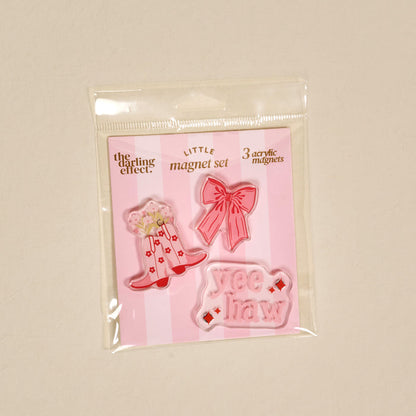 The Darling Effect Howdy Honey Little Magnet Set includes three acrylic magnets—a pink cowboy hat with flowers, a pink bow, and a pink "Yee Haw" sign—ideal as decorative accents or fridge magnets. Packaging reads: LITTLE magnet set 3 acrylic magnets.