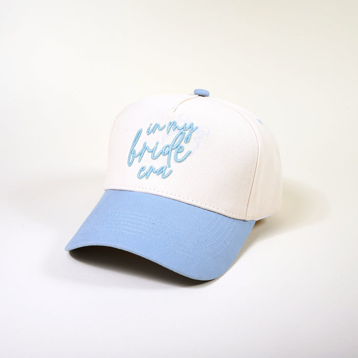 The Darling Effect’s In My Bride Era Classic Canvas Hat features an off-white crown with “in my bride era” embroidered in light blue, a matching brim and button, perfect for everyday wear. Displayed on a plain, light background.