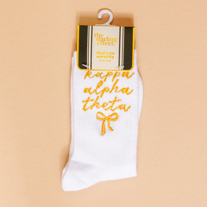 Kappa Alpha Theta Embroidered Crew Socks by The Darling Effect feature gold script and a small gold bow, making them the perfect sorority gift. Includes yellow and black "the darling effect" tag.