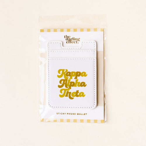 The Darling Effect's Kappa Alpha Theta Stick-On Phone Wallet features white material with gold lettering, packaged in clear plastic with a yellow and white striped border—an ideal sorority gift or phone accessory for Theta sisters.