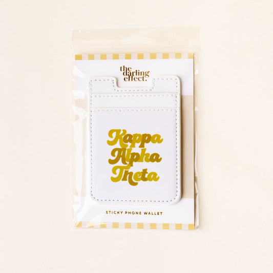 The Darling Effect's Kappa Alpha Theta Stick-On Phone Wallet features white material with gold lettering, packaged in clear plastic with a yellow and white striped border—an ideal sorority gift or phone accessory for Theta sisters.
