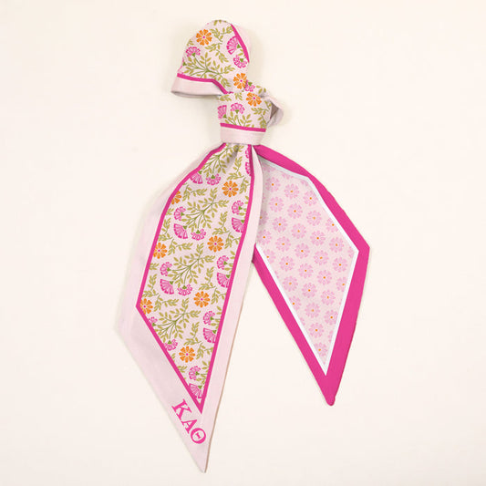 The Darling Effect’s Kappa Alpha Theta Twirl & Tie Scarf Accessory features pink, yellow, and green florals on one side, a pink geometric print on the other, and ΚΑΘ Greek letters in the corner—perfect for adding boutique charm.