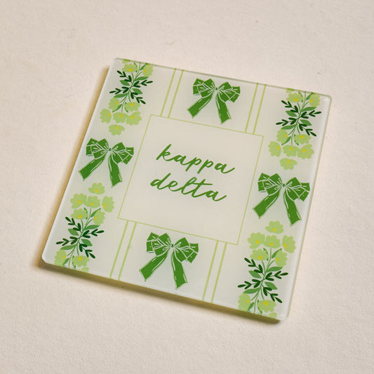 The Darling Effect's Kappa Delta Acrylic Coaster features green bows, floral designs, and “kappa delta” in green script—perfect for sisterhood gifts or showing chapter pride. Ideal for light surfaces.