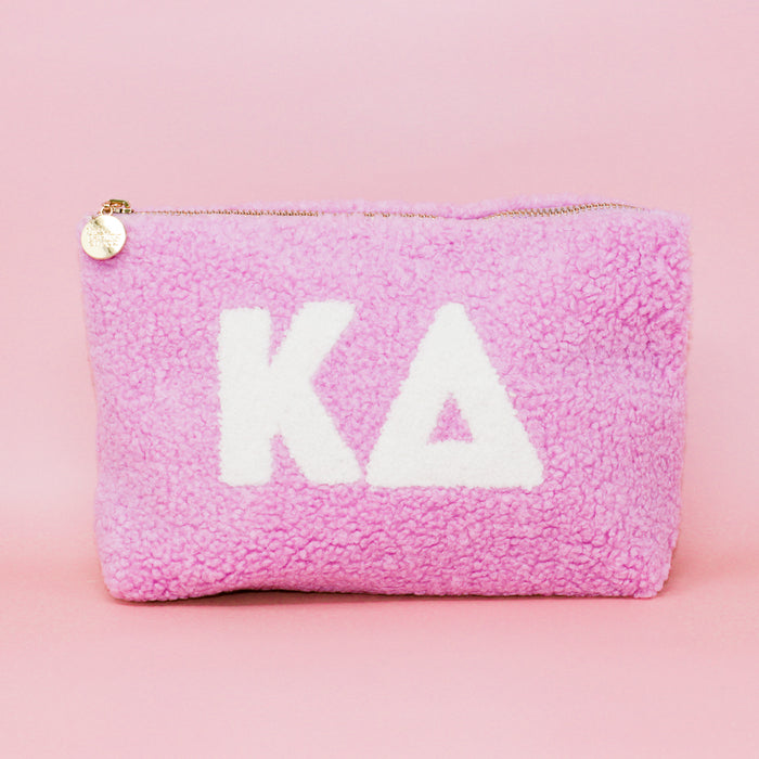 Introducing the Kappa Delta Lilac Teddy Letter Pouch by The Darling Effect—a soft sherpa pouch in delicate lilac, featuring crisp white Greek letters for Kappa Delta on the front. Accented with a gold zipper and a round charm, this stylish accessory is perfect as a teddy pouch or chic carry-on essential.