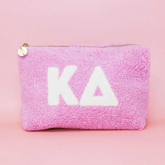 Introducing the Kappa Delta Lilac Teddy Letter Pouch by The Darling Effect—a soft sherpa pouch in delicate lilac, featuring crisp white Greek letters for Kappa Delta on the front. Accented with a gold zipper and a round charm, this stylish accessory is perfect as a teddy pouch or chic carry-on essential.