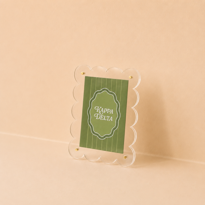 The Darling Effect's Kappa Delta Mini Acrylic Picture Frame Magnet features a scalloped clear acrylic frame displaying a green Kappa Delta card in white lettering on a light beige background.