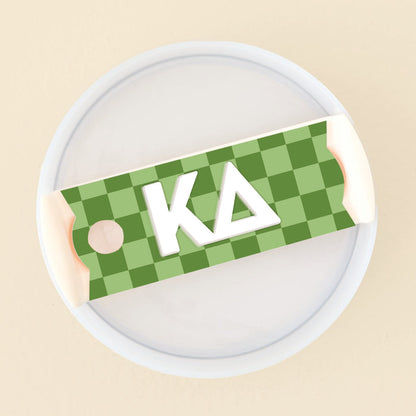 The Darling Effect Kappa Delta Tumbler Lid Tag features a green checkered design with white edges and the Greek letters KΔ in white, shown atop a round white tumbler lid—ideal for personalizing your sorority drinkware.