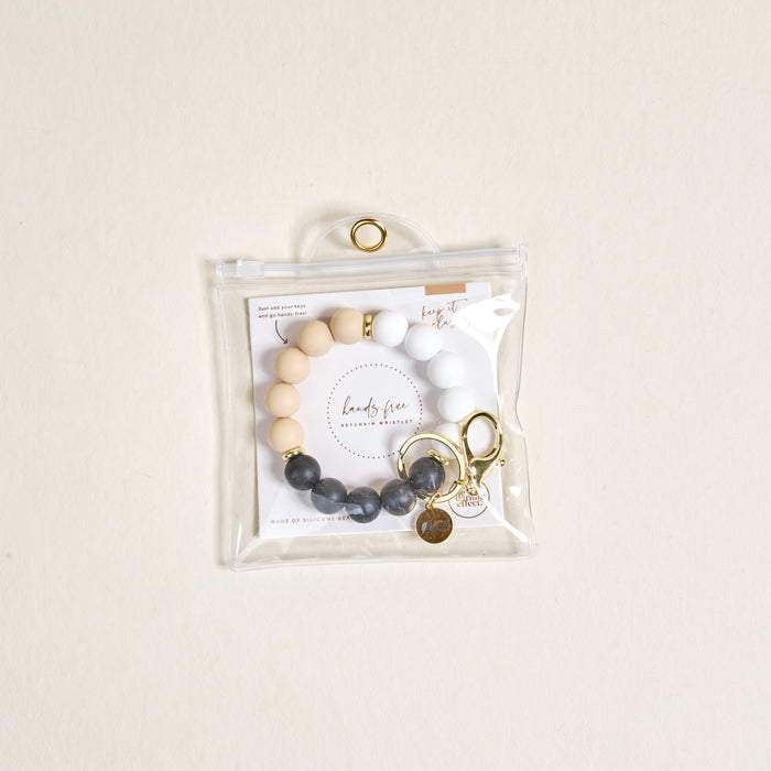 The Darling Effect Keep It Classy Hands-Free Keychain Wristlet features beige, white, and gray silicone beads with gold accents, a keyring, and comes in a clear zippered pouch for easy, stylish access.