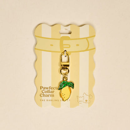 The Lemon Pawfect Collar Charm by The Darling Effect is a gold and yellow lemon-shaped accessory with green leaves. Attached to striped "Pawfect Collar Charm" packaging, it adds playful style to any pet collar and stands out among must-have accessories.