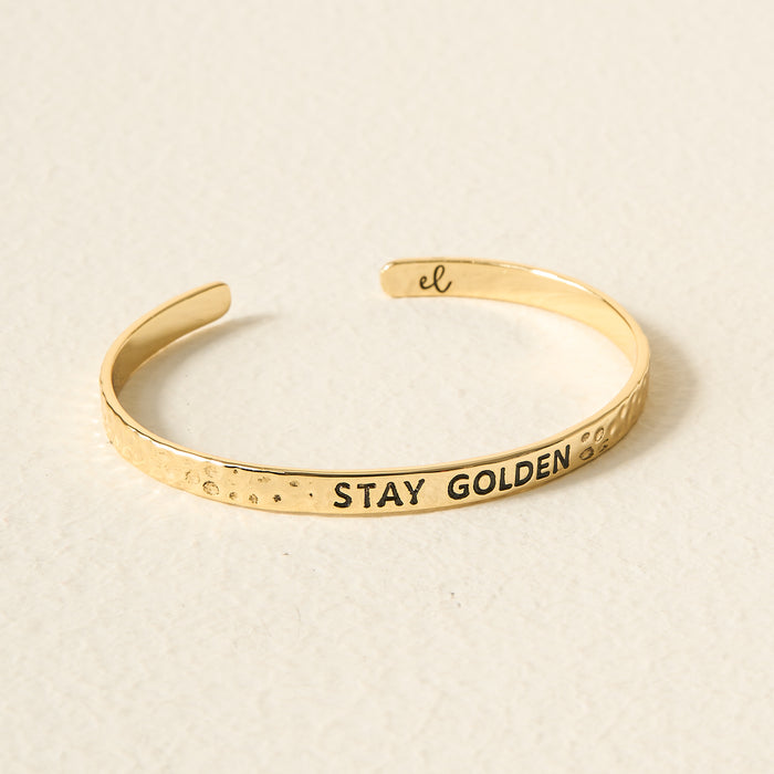 The Darling Effect’s Little Reminder Cuff is a hammered 14k gold adjustable bracelet inscribed with STAY GOLDEN and the el logo—a daily mantra accessory for inspiration.