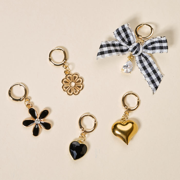 Five gold huggie charm earrings—black enamel daisy, gold flower, black crystal heart, gold puffy heart, and black-and-white gingham bow with crystal drop—by The Darling Effect’s Midnight Moments The Ultimate Charm Pack. Mix and match with your favorites!.