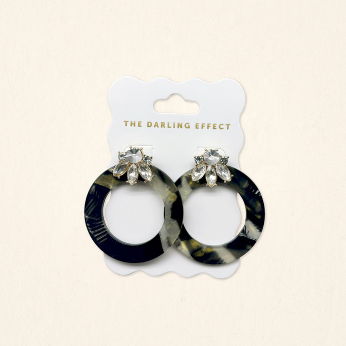 The Darling Effect's Midnight Opal Glow Getter Earrings showcase a black, white, and gold marbled acetate design with clear teardrop accents—lightweight statement earrings perfect for any occasion.