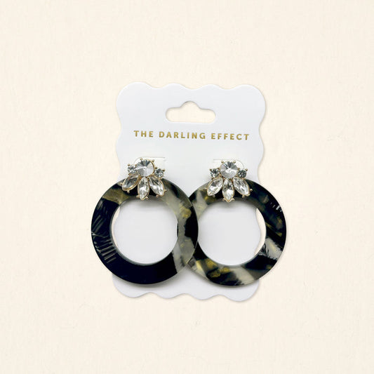 The Darling Effect's Midnight Opal Glow Getter Earrings showcase a black, white, and gold marbled acetate design with clear teardrop accents—lightweight statement earrings perfect for any occasion.