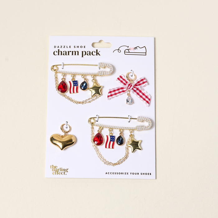 Add patriotic flair to your footwear with The Darling Effect’s Miss Americana Dazzle Shoe Charm Pack—featuring red, white, and blue sneaker charms, gold stars, and a gem-topped checkered bow. Perfect for American-themed style!.