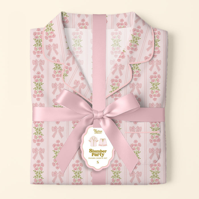 The Darling Effect’s Oh So Fancy Pink Slumber Party Pajama Shorts Set features a floral and bow pattern, ultra-soft fabric, and arrives gift-ready with a pink satin ribbon and a tag reading "Slumber Party Pajama Gift Set.