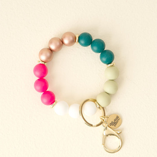 The Darling Effect’s Oh What Fun Hands-Free Keychain Wristlet features stylish pink, white, rose gold, teal, and light green silicone beads with a gold keyring, lobster clasp, and chic round charm for effortless style on the go.