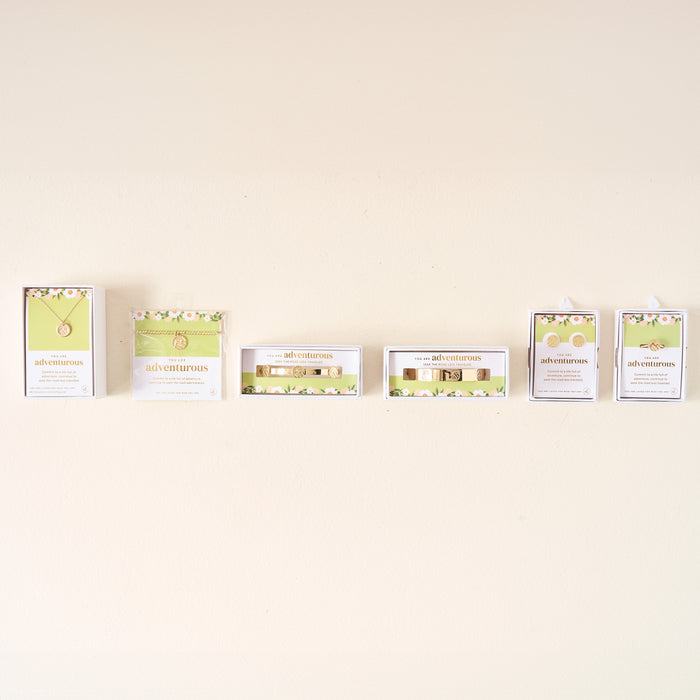 Five jewelry gift sets from The Darling Effect in light green and white floral boxes are displayed on a beige wall. Each set features an Original Trait Cuff Bracelet or other sterling silver piece like a necklace, bracelet, or earrings.