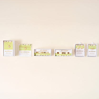 Five jewelry gift sets from The Darling Effect in light green and white floral boxes are displayed on a beige wall. Each set features an Original Trait Cuff Bracelet or other sterling silver piece like a necklace, bracelet, or earrings.