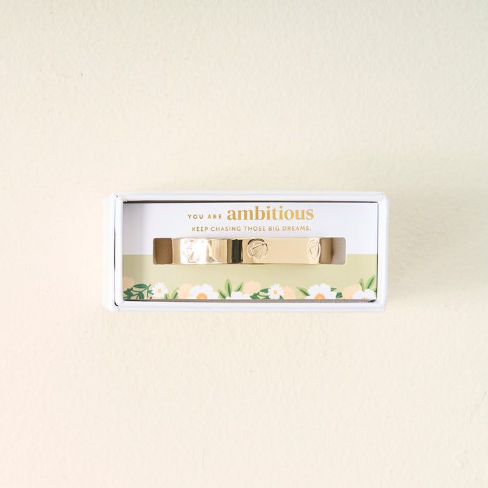 The Darling Effect's Original Trait Cuff Bracelet comes in a white floral box with a card that reads, "You are ambitious. Keep chasing those big dreams." This gold adjustable bracelet features small engraved symbols for extra charm.