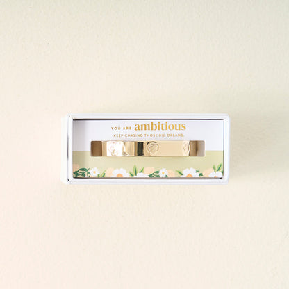 The Darling Effect's Original Trait Cuff Bracelet comes in a white floral box with a card that reads, "You are ambitious. Keep chasing those big dreams." This gold adjustable bracelet features small engraved symbols for extra charm.