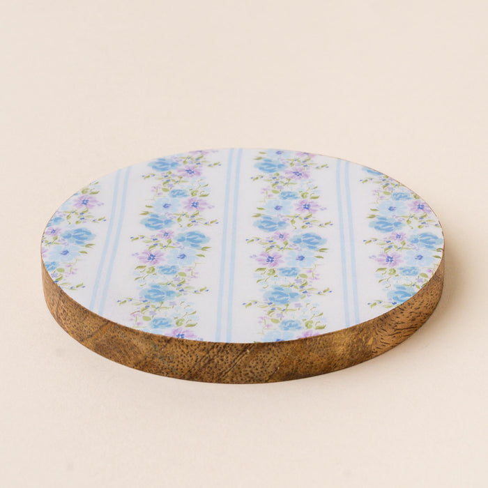 The Petal Parade Blue Wood Enamel Coaster by the-darling-effect features a white top with blue and purple floral patterns and vertical stripes, blending style and function to protect your table while adding charm to any space.