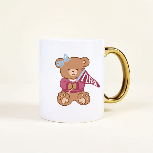The Darling Effect's Pi Beta Phi 11 oz Cozy Cute Ceramic Mug features a gold handle and an adorable teddy bear in a pink sweater with a maroon ΠΒΦ pennant—an ideal sorority mug or gift.