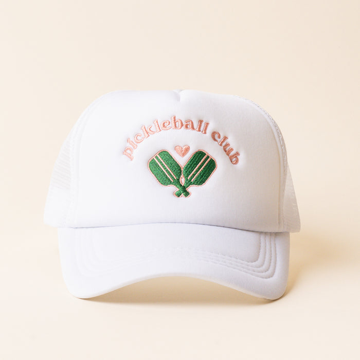 The Pickleball Club Trucker Hat by the-darling-effect features trendy pink "pickleball club" embroidery, crossed green paddles, and a pink heart on a white hat with a light beige background—perfect for sporty, playful style lovers.