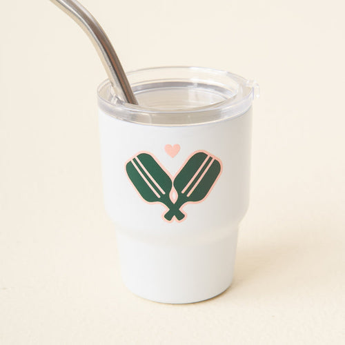 The Pickleball Paddles 2 oz Tiny Tumbler by the-darling-effect is a white insulated cup with a clear lid and metal straw, featuring two green pickleball paddles crossed with a pink heart—ideal for fans of cute mini tumblers.
