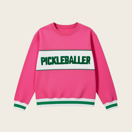 The Darling Effect’s Pickleballer Signature Crew is a bright pink sweatshirt with white and green sleeve and hem stripes, soft fabric, and a bold green PICKLEBALLER print on a white chest panel.