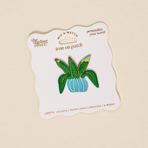 The Darling Effect’s Plant Mix & Match Iron-On Patch showcases a green and gold plant in a blue pot on a white backing—ideal for customizing your style with vibrant flair.