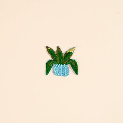 Add a touch of nature to your look with The Darling Effect’s Plant Mix & Match Iron-On Patch—a green potted plant with long leaves in a light blue pot, perfect for personalizing your style.