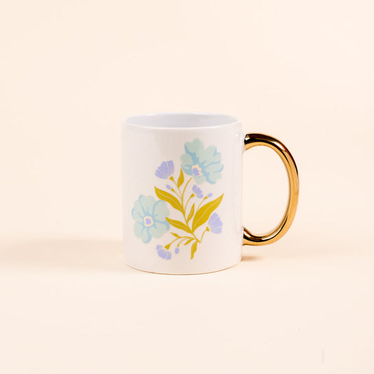 The Darling Effect's Poppin' Petals Aqua 11 oz Cozy Cute Ceramic Mug features a floral motif with light blue flowers and yellow-green leaves, plus a golden handle—perfect for enjoying coffee or tea.