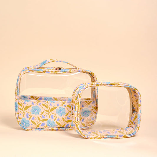 The Darling Effect’s Poppin' Petals Aqua Clearly Chic Cosmetic Bag Set features two clear bags with blue and purple floral trim on peach, including a large travel bag with top handle and zipper, plus a matching square pouch.