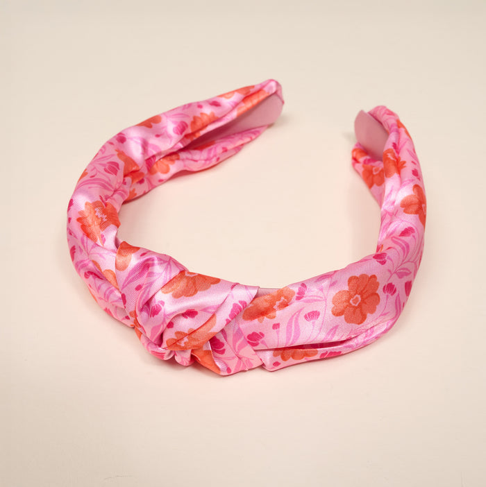 The Darling Effect's Poppin' Petals Hot Pink Classic Twist Headband features a pink satin floral pattern in pink and orange, shown on a light beige background—a chic, versatile accessory for any occasion.