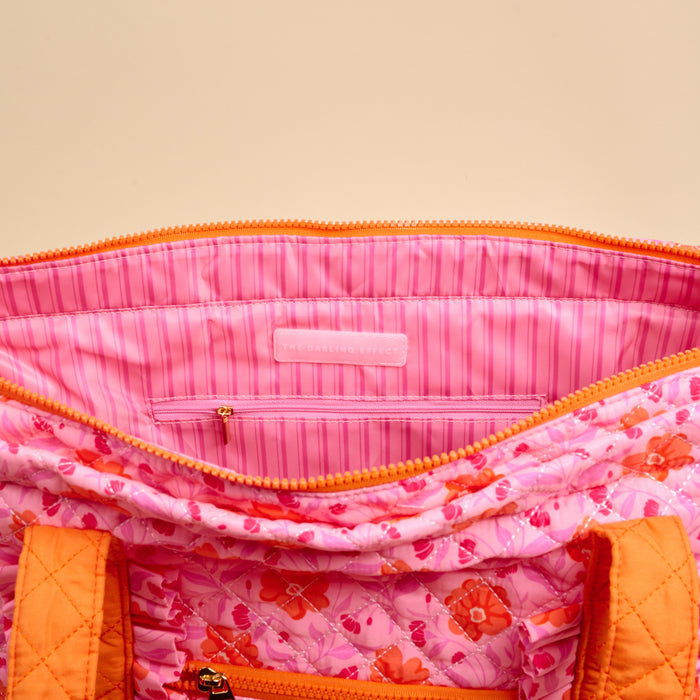 A close-up of The Darling Effect's Poppin' Petals Hot Pink The Everyday Quilted Tote Bag, featuring orange zippers, a pink striped lining, and an inner pocket—ideal as a colorful travel or everyday tote.