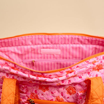 A close-up of The Darling Effect's Poppin' Petals Hot Pink The Everyday Quilted Tote Bag, featuring orange zippers, a pink striped lining, and an inner pocket—ideal as a colorful travel or everyday tote.