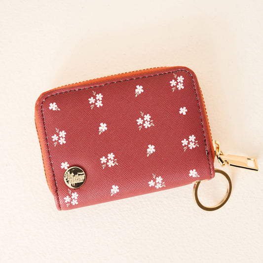 The Darling Effect Pretty Posies Cognac Zip Around Wallet is a compact cognac keyring wallet with gold zipper, card slots, tiny white flower pattern, and a round gold emblem at the bottom left, shown against a light background.