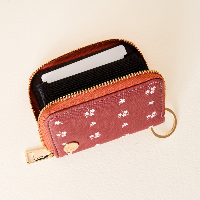The Darling Effect Pretty Posies Cognac Zip Around Wallet, featuring a white floral pattern, gold zipper, and keyring design, is open to reveal card slots and a blank card inside.