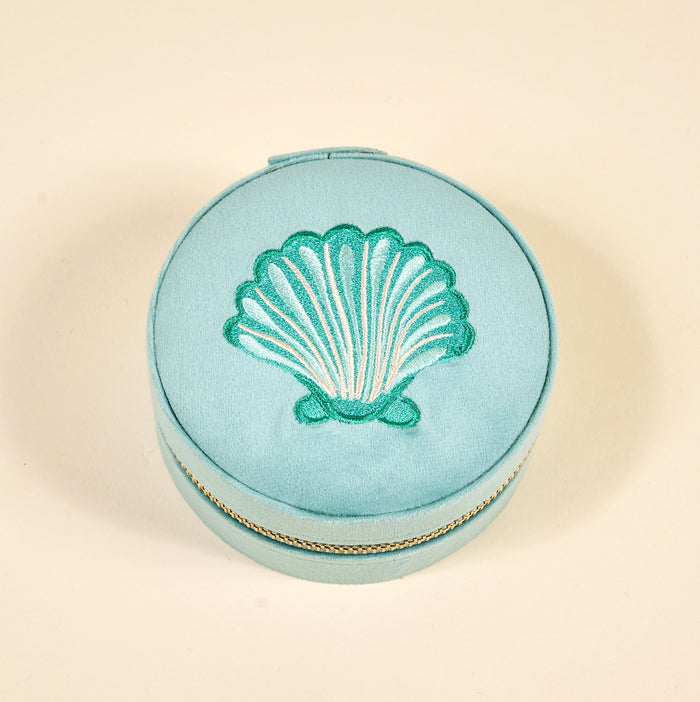 The Darling Effect's Seashell Round Velvet Jewelry Case features light blue velvet, a green embroidered seashell on the lid, and a gold zipper—an elegant ring holder shown against a plain beige background.