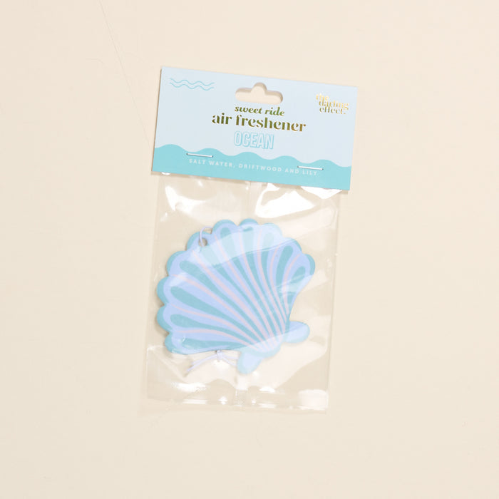 The Darling Effect's Seashell Sweet Ride Car Air Freshener offers a unique salt water, driftwood, and lily scent. Housed in clear packaging with blue and white accents, it guarantees a long-lasting ocean-inspired aroma for your drive.