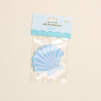 The Darling Effect's Seashell Sweet Ride Car Air Freshener offers a unique salt water, driftwood, and lily scent. Housed in clear packaging with blue and white accents, it guarantees a long-lasting ocean-inspired aroma for your drive.