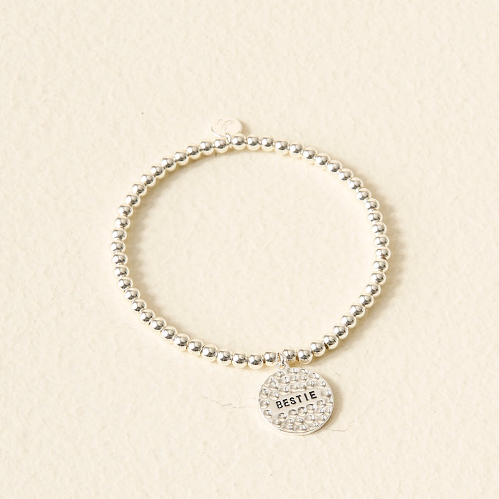 The Darling Effect Sentiment Beaded Charm Bracelet features silver beads and a round BESTIE charm—displayed on a light, textured background—a thoughtful gift for your closest friend.