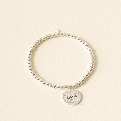 The Darling Effect Sentiment Beaded Charm Bracelet features silver beads and a round BESTIE charm—displayed on a light, textured background—a thoughtful gift for your closest friend.