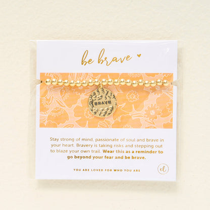 The Darling Effect Sentiment Beaded Charm Bracelet features gold beads and a round BRAVE charm, displayed on a floral card with "be brave"—a thoughtful gift that inspires bravery and self-love.