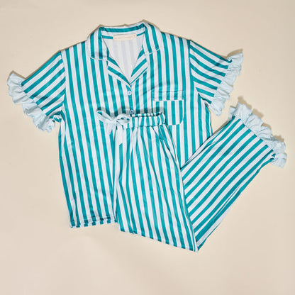 The Darling Effect Sicily Stripes Teal Slumber Party Pajama Pants Set features blue and white vertical stripes, ruffled short sleeves and pant legs, a button-up top with chest pocket, and matching pants—all displayed flat on a cream background.